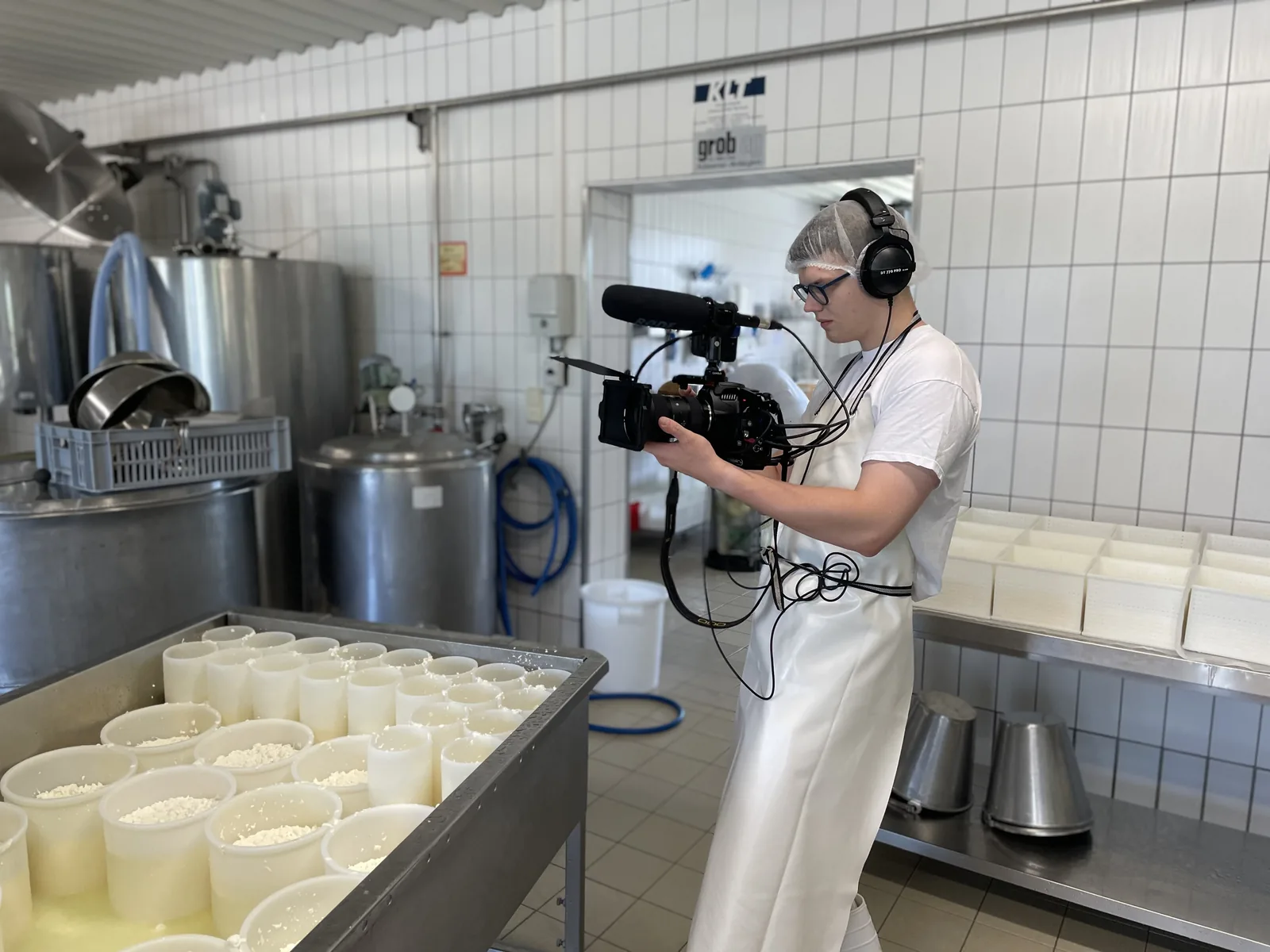 Kameraaufnahme neben Käseformen und Edelstahlbehältern in einer Molkerei.