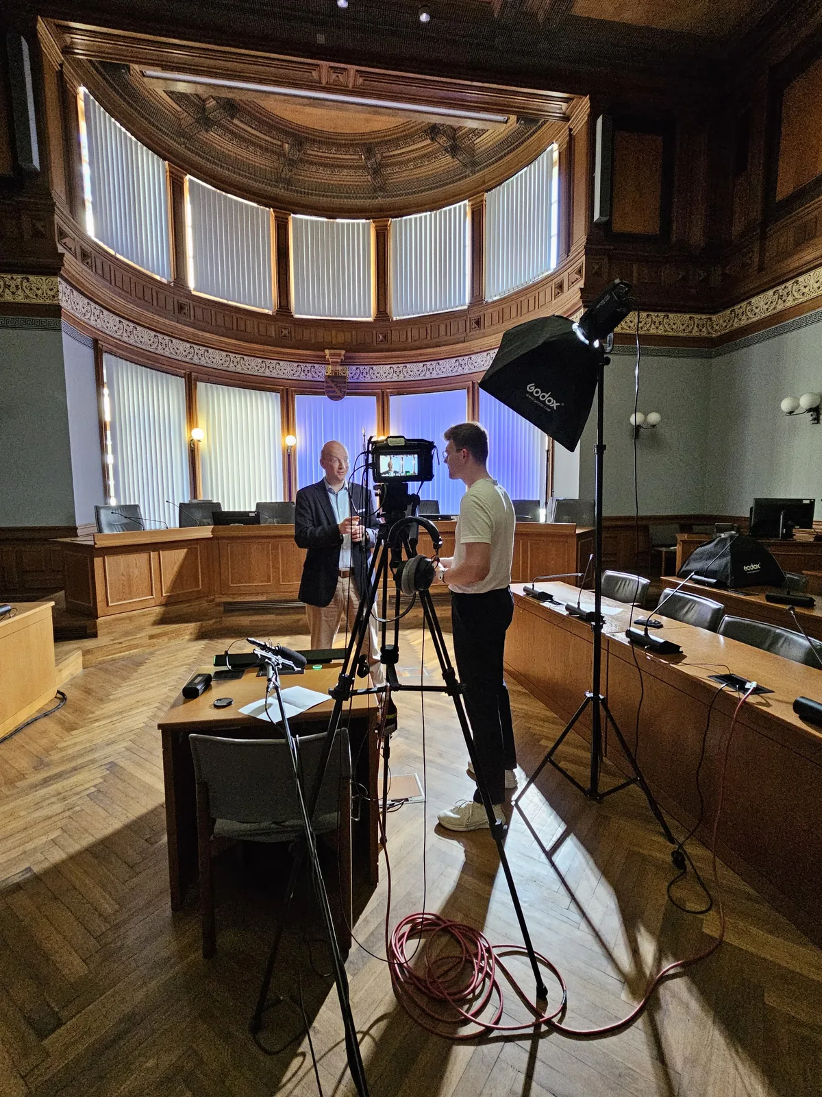 Kameras und Stative in einem Saal mit geschwungener Holzvertäfelung.