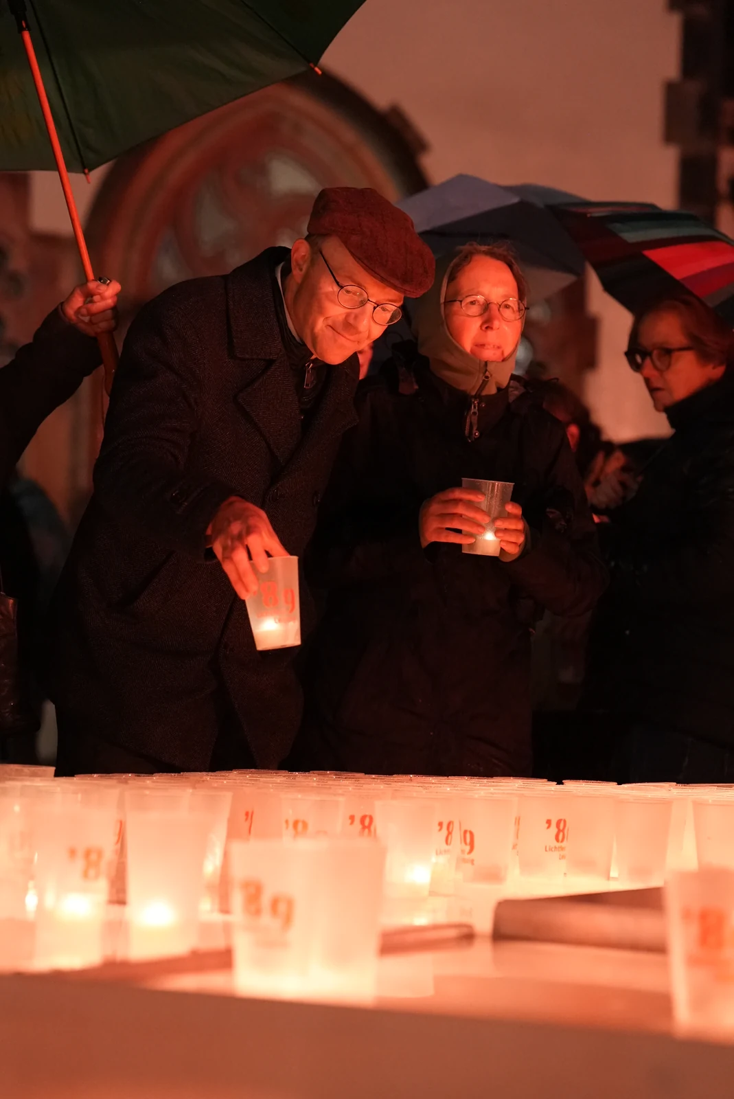 Menschen mit Kerzen unter Regenschirmen bei einer Abendveranstaltung.